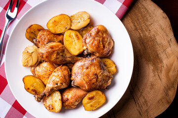 Chicken baked in pieces with potatoes and onion on a white dish.