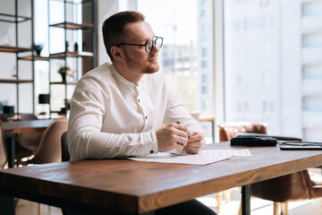 Handsome talented young composer wearing stylish eyeglasses is writing musical notes with pen on...