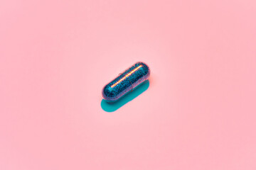 Creative concept with blue glitter pill isolated on pastel pink background. Minimal style, art concept - obrazy, fototapety, plakaty