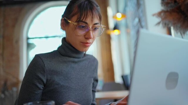 camera zooming out woman working at laptop in cafe, pensive woman freelancer noting information for planning project doing remote job via laptop computer