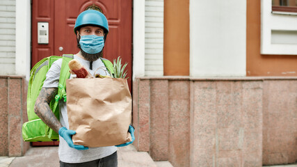 Bearded delivery man in helmet wearing mask and gloves due to the emergence of the Covid19 virus,...
