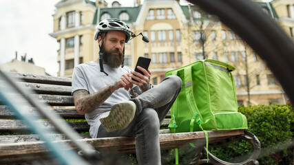 Accepting orders. Brutal bearded delivery man in helmet with thermo bag or backpack checking order...