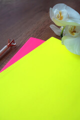 A greensand a pink notebook with a pencil and a white orchid are standing on a wooden table.
