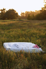 idea for a photo shoot in nature. bed with bed linen in a field in the summer at sunset