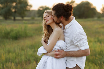 the couple is in love and kissing in the field in the summer. soft sunlight.