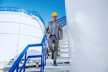 Young successful attractive caucasian businessman in suit with helmet on head going down the stairs...