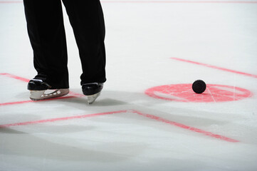 Ice hockey referee standing on ice. Closeup of referee trousers and skates. Face-off spot and a...