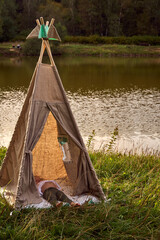 Girl at sunset in nature. Wigwam by the lake. New home in a hut. CHILDREN'S GAMES. High quality...
