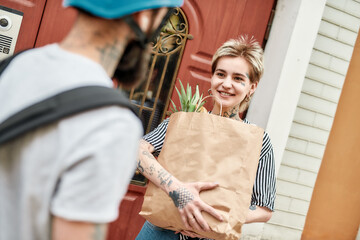 Delivery man with backpack giving away grocery bag to happy female customer, while delivering food. Courier, delivery service concept