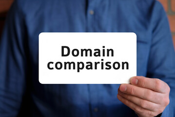 Domain comparison text on a white sign in the hand of a man in a blue shirt