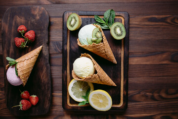 Various flavored ice cream scoops in waffle cones on wooden table. Food background, summer refreshment concept