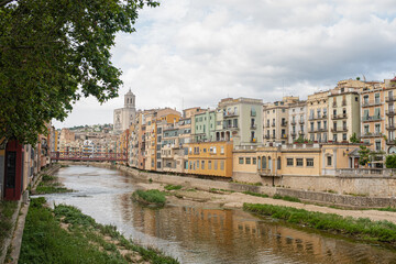 Fototapeta premium Girona's skyline on a cloudy day with water reflection river houses, bridge and massive cathedral on the horizon