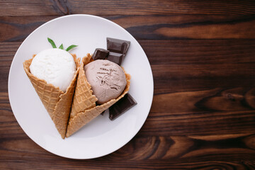Ice cream set of chocolate and vanilla flavored scoops in waffle cones on white plate. Food background, summer refreshment concept