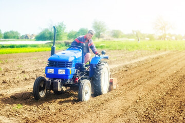 Fototapeta premium A farmer on a tractor cultivates a farm field. Agriculture, growing organic food vegetables. Soil milling, crumbling and mixing. Loosening the surface, cultivating the land for further planting.