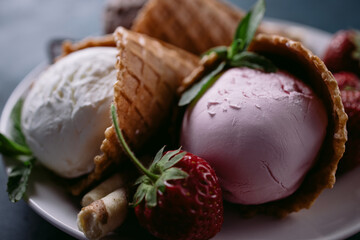 Ice cream set of strawberry, chocolate and vanilla flavored scoops in waffle cones on white plate, close up. Delicious summer snacks