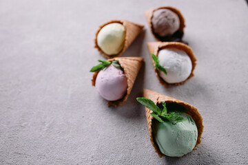 Various flavored ice cream scoops in waffle cones on stone table. Food background, summer refreshment concept