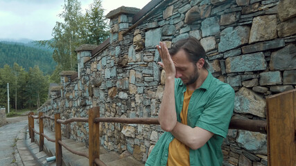 Depressed man smoking cigarette, feeling disappointed, standing along the road, stone wall on background. Male with bad habit.