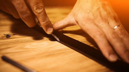Working process of the leather belt in the leather workshop. Man holding tool. Tanner in old tannery. Wooden table background. Close up man arm. Warm Light for text and design. Web banner size