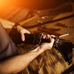 Working process of the leather craft in the workshop. Man holding photographer's belt for camera. Wooden background. Tanner in old tannery.Close up arms.Warm Light for text and design. Web banner size