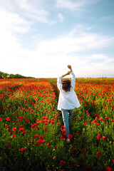 Young girl in hat posing in the poppy field. Portrait of curly girl walking in poppy field at sunset. Summertime.