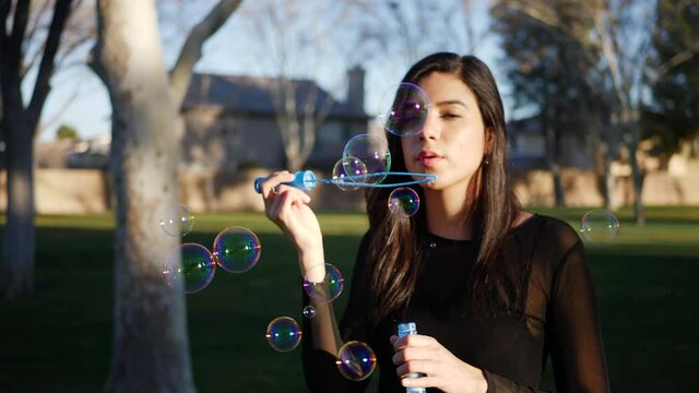A beautiful girl blowing many dreamy bubbles in sunlight while smiling in a joyful way SLOW MOTION.