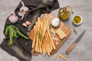 Traditional italian breadsticks grissini with rosemary, parmesan cheese, olive oil, garlic and salt on a gray background. top view. Flat lay with copy space