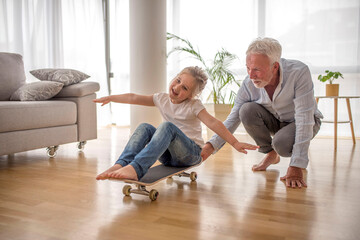 Granddaughter having fun while riding skateboard at home with her grandfather