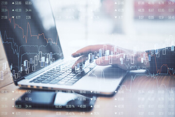 Hands using laptop on desktop with abstract forex chart