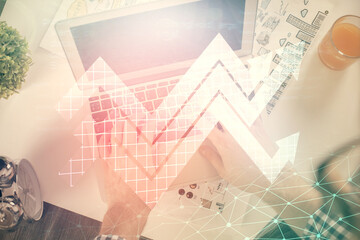 Obraz premium Double exposure of man's hands typing over computer keyboard and growing arrows hologram drawing. Top view. Success concept.