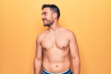 Fototapeta premium Young handsome man with beard wearing sleeveless t-shirt standing over yellow background looking away to side with smile on face, natural expression. Laughing confident.