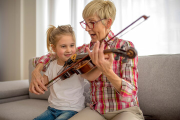 Grandmother teaching her granddaughter to play violin at home © Drpixel