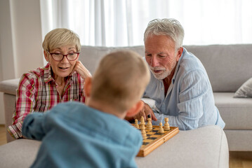 Happy grandparents playing chess with their grandson at home