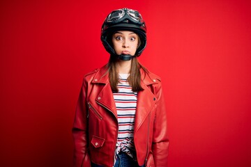 Young beautiful brunette motocyclist woman wearing motorcycle helmet and red jacket puffing cheeks with funny face. Mouth inflated with air, crazy expression.