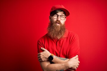 Young handsome delivery man wearing glasses and red cap over isolated background shaking and freezing for winter cold with sad and shock expression on face