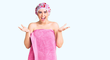 Young caucasian woman wearing shower cap and towel celebrating victory with happy smile and winner expression with raised hands