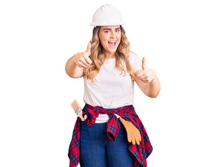 Young caucasian woman wearing security helmet approving doing positive gesture with hand, thumbs up...