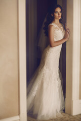 Fototapeta premium The morning of the bride. Beautiful girl in a white dress is preparing for the wedding ceremony. The beautiful young woman posing in a wedding dress. Fashion portrait of a beautiful bride