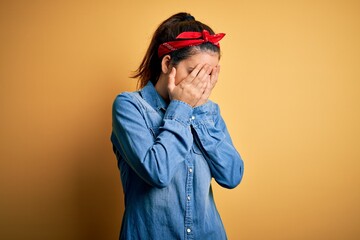 Young beautiful brunette woman wearing casual denim shirt and hair handkerchief with sad expression covering face with hands while crying. Depression concept.