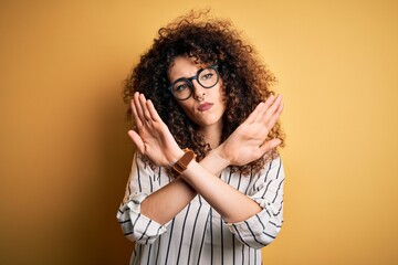 Young beautiful woman with curly hair and piercing wearing striped shirt and glasses Rejection expression crossing arms doing negative sign, angry face