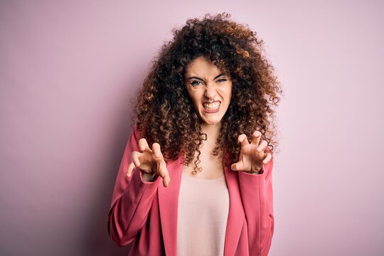 Young beautiful businesswoman with curly hair and piercing wearing elegant jacket smiling funny doing claw gesture as cat, aggressive and sexy expression