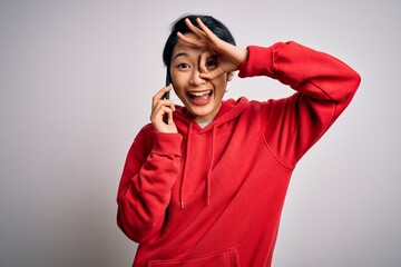 Young beautiful asian girl having conversation talking on the smartphone over white background with happy face smiling doing ok sign with hand on eye looking through fingers