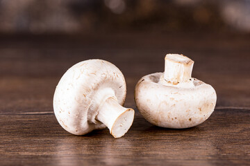 Two fresh white mushrooms champignon on wooden table.