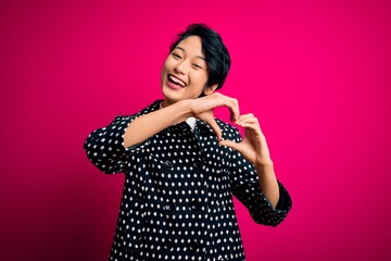Young beautiful asian girl wearing casual jacket standing over isolated pink background smiling in love doing heart symbol shape with hands. Romantic concept.