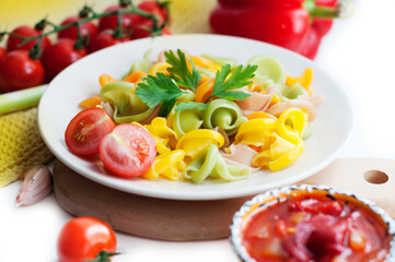 Colorful pasta with tomatoes, garlic, parsley, pepper on a white plate. Pasta for child with tomato sauce on a white background