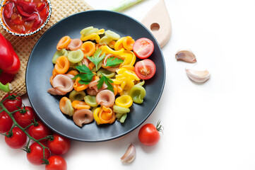 Colorful pasta with tomatoes, garlic, parsley, pepper on a black plate. Pasta for child with tomato sauce on a white background. Top view