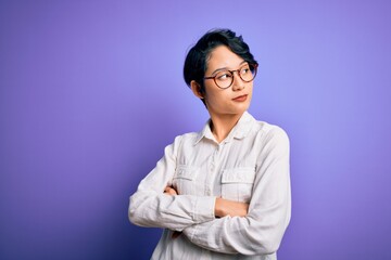 Young beautiful asian girl wearing casual shirt and glasses standing over purple background looking...