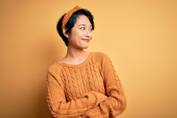 Young beautiful asian girl wearing casual sweater and diadem standing over yellow background...