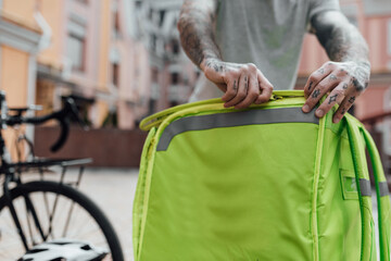 Fast, Fresh, Instant. Close up of delivery man closing thermo bag or backpack to be ready to go, standing outdoors with bike. Courier, delivery service concept