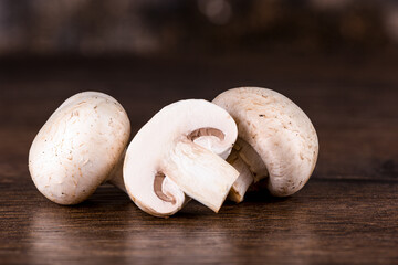 Two fresh champignon mushrooms and a cut mushroom on a wooden table
