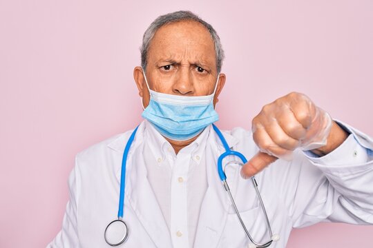 Senior Hoary Doctor Man Wearing Medical Mask And Stethoscope Over Pink Background With Angry Face, Negative Sign Showing Dislike With Thumbs Down, Rejection Concept